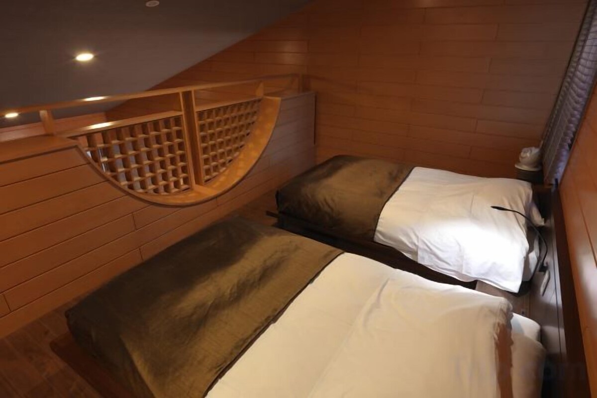 A compact room with two beds, wooden walls, and a sloped ceiling.