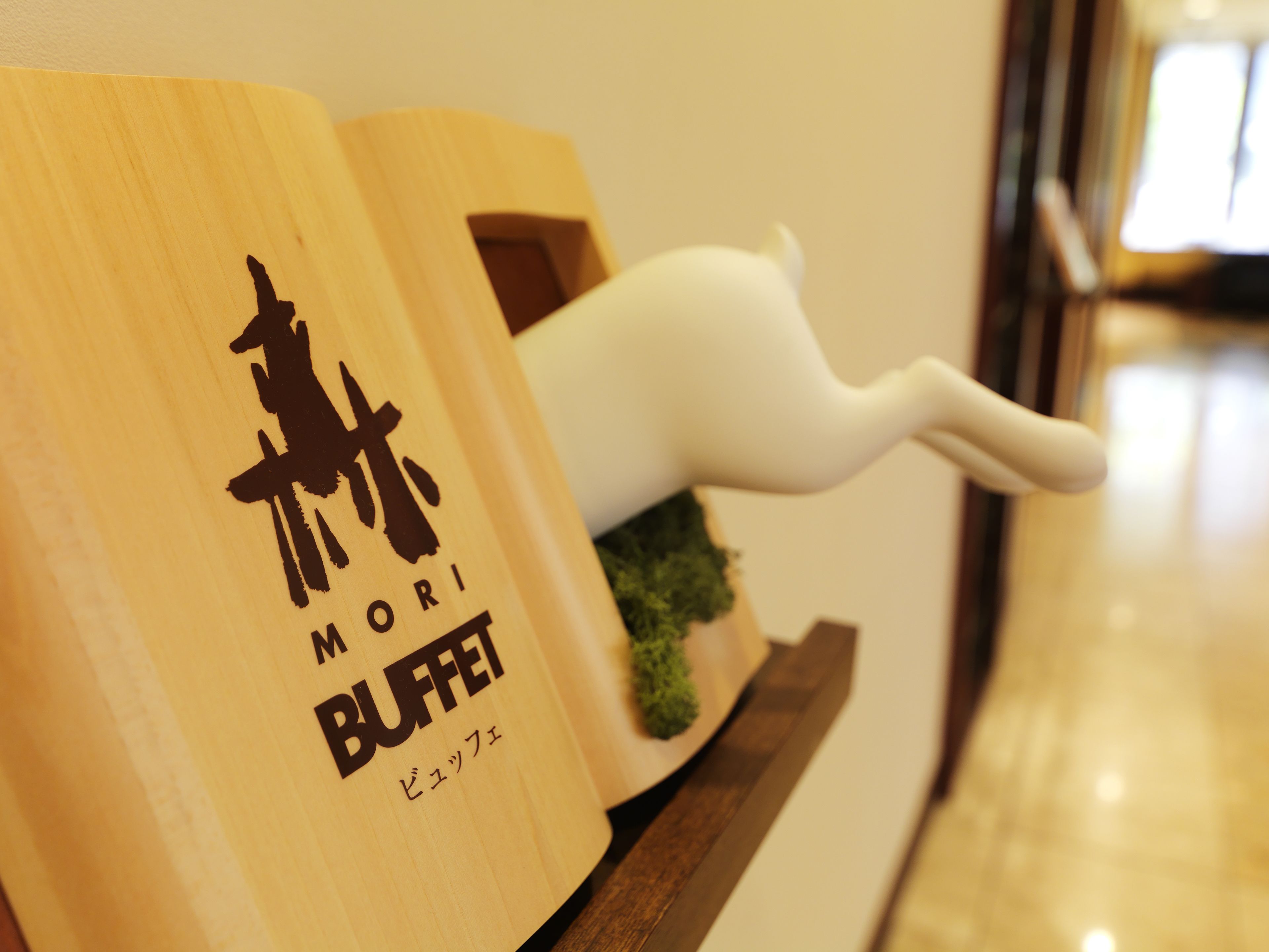 Un letrero de madera para un bufé con una tetera blanca y una pequeña planta verde.