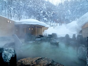 A hot spring area with stone seating and a wooden structure, surrounded by snow-covered trees. - Jozankei Tsuruga Resort Spa MORI no UTA (Sapporo)