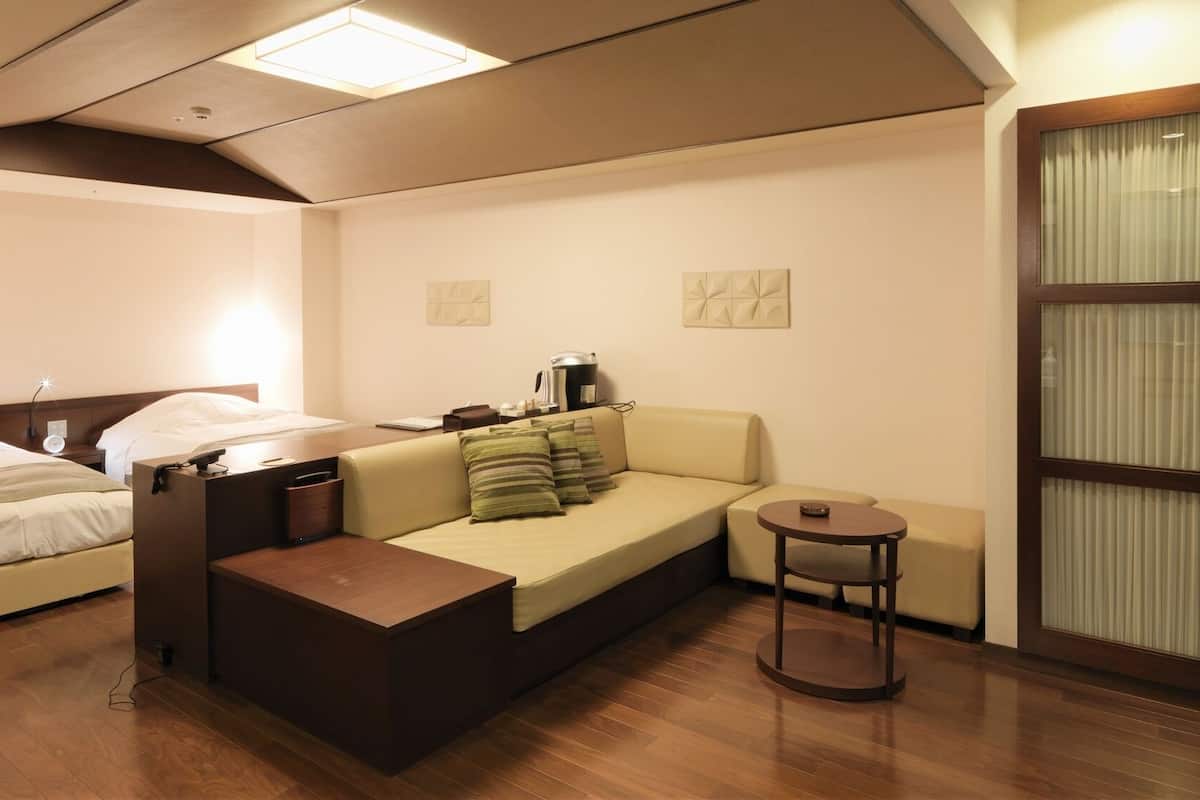 A compact hotel room with a bed, a sofa, a small table, and a coffee machine.