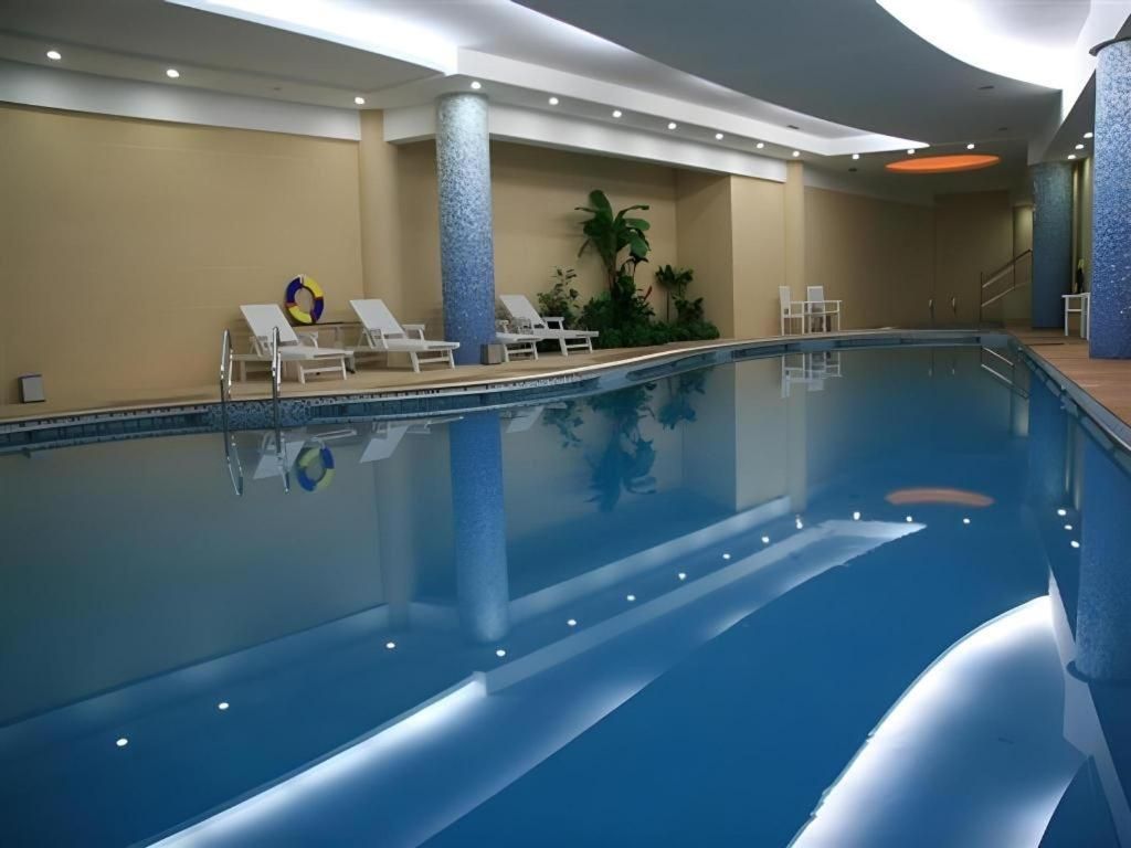 An indoor swimming pool with lounge chairs, a lifebuoy, and a staircase leading to a higher level.