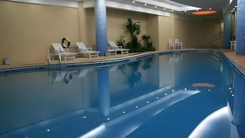 An indoor swimming pool with lounge chairs, a lifebuoy, and a staircase leading to a higher level.