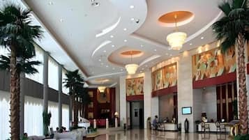 A spacious lobby with a high ceiling, palm trees, and a reception desk.
