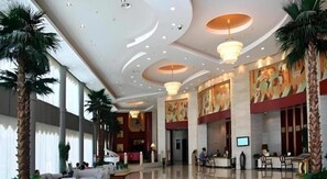 Un vestíbulo amplio con techo alto, palmeras y una mesa de recepción.
