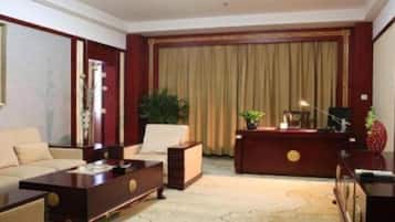 A hotel room with a sofa, a desk, a chair, a coffee table, and a large window with curtains.