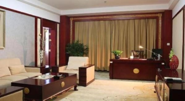 Une chambre d’hôtel équipée d’un canapé, d’un bureau, d’une chaise, d’une table basse et d’une grande fenêtre avec des rideaux.