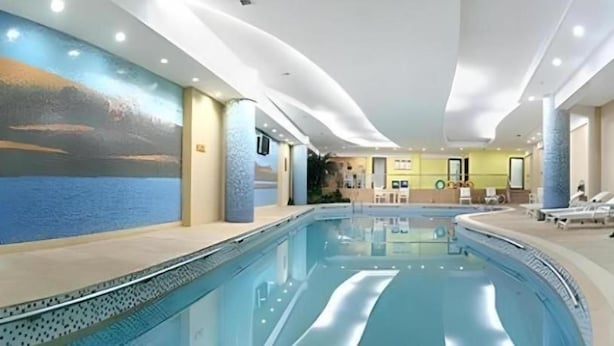 An indoor swimming pool with a view of the sea through a mural, a reception area, and lounge chairs. - Grand Soluxe Hotel Dunhuang (Jiuquan)