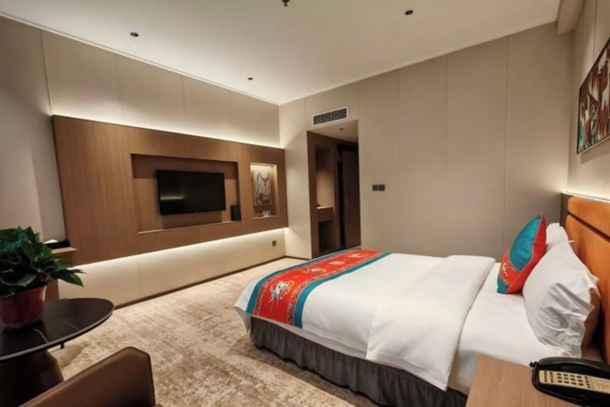 Una habitación de hotel con una cama, un televisor montado en la pared, un escritorio con un teléfono y una planta en maceta.