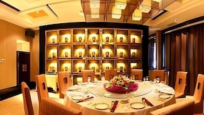 A round dining table with chairs, a floral centerpiece, and a wall with illuminated shelves. - Grand Soluxe Hotel Dunhuang (Jiuquan)