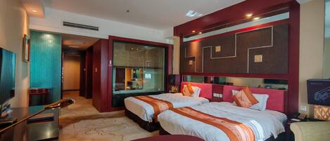 A hotel room with two beds, a desk, a chair, and a television.