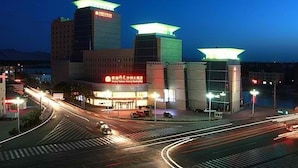 A multi-story building with illuminated top sections, a crosswalk, and a busy street with light trails. - Grand Soluxe Hotel Dunhuang (Jiuquan)