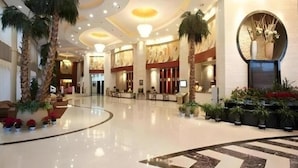 A spacious lobby with a curved floor, reception desk, and decorative plants. - Grand Soluxe Hotel Dunhuang (Jiuquan)