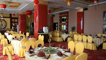 A banquet hall with round tables, yellow chairs, and red lanterns.