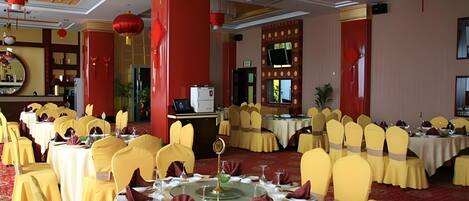 A banquet hall with round tables, yellow chairs, and red lanterns.