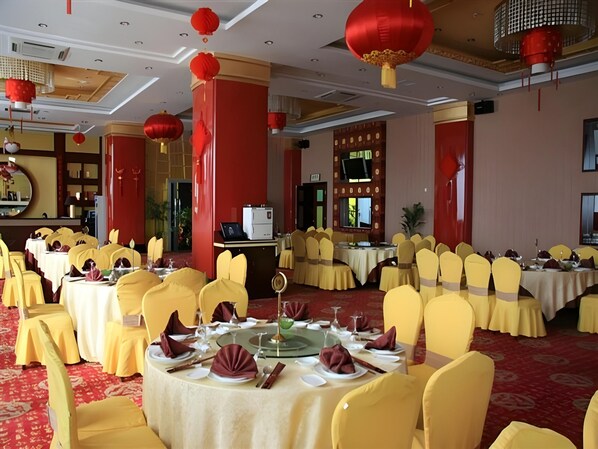 Un salón de banquetes con mesas redondas, sillas amarillas y faroles rojos.
