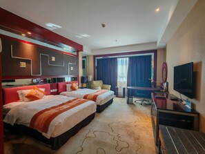 Habitación de hotel con dos camas, un escritorio, un televisor y un ventanal grande con cortinas.