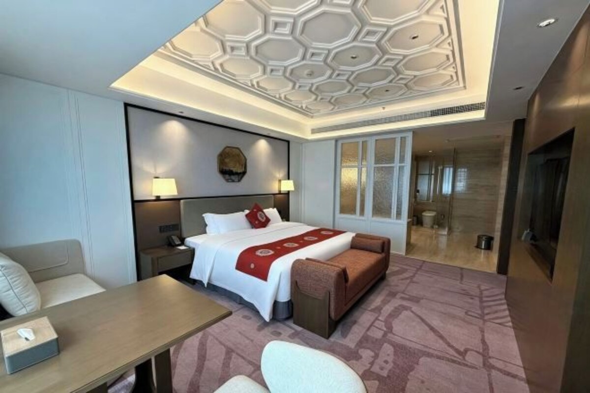 Habitación de hotel con cama, sofá, mesa y techo con diseño geométrico.