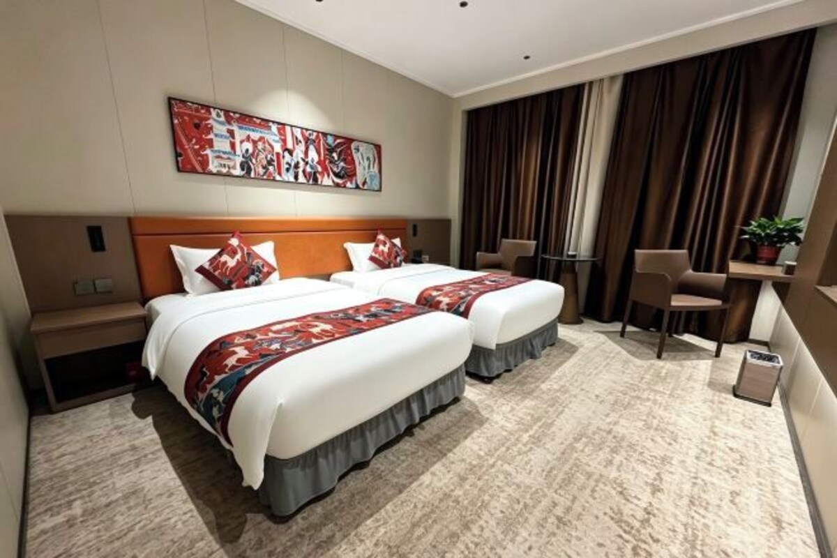 Una habitación de hotel con dos camas, un escritorio, una silla y un ventanal con cortinas.
