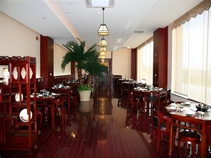 Un restaurant spacieux avec de hauts plafonds, de nombreuses tables et une plante décorative au centre.