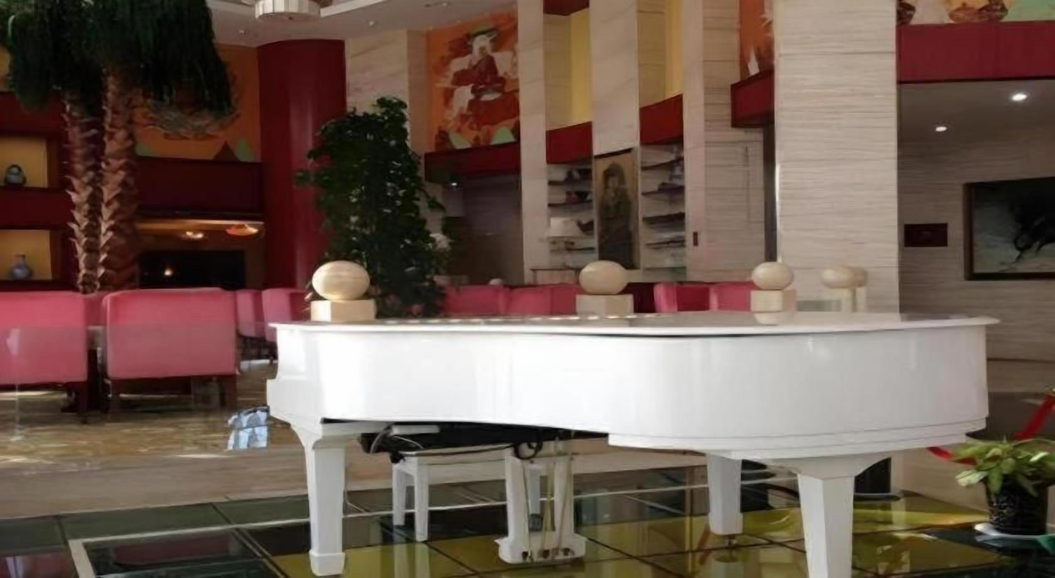A white grand piano in a lobby with red seating and a large plant.