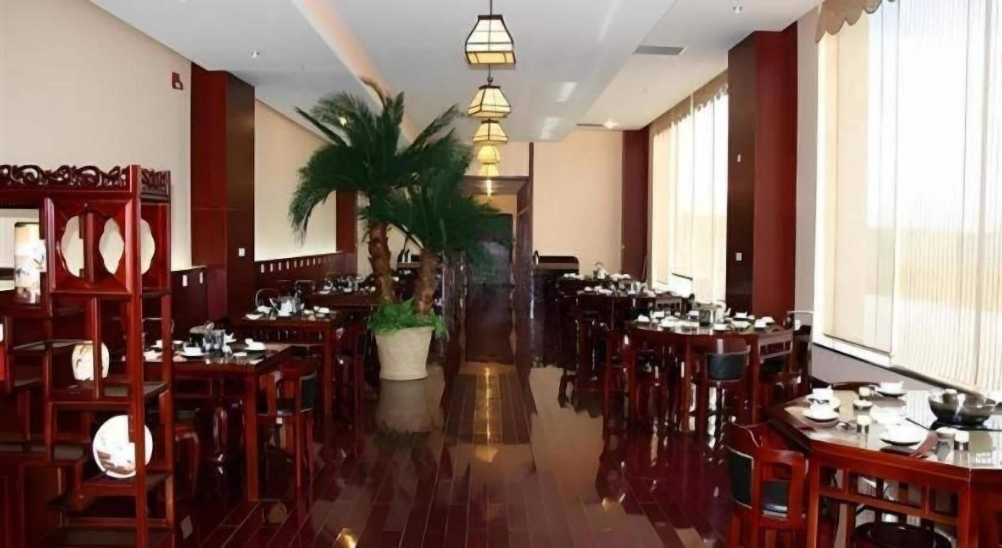 A spacious dining area with multiple tables and chairs, a central plant, and a chandelier.