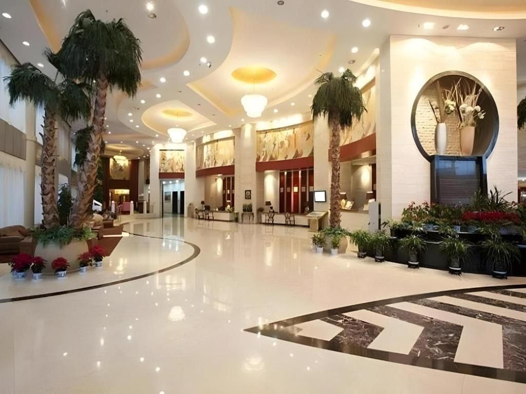 A spacious lobby with a polished floor, palm trees, and a reception desk.