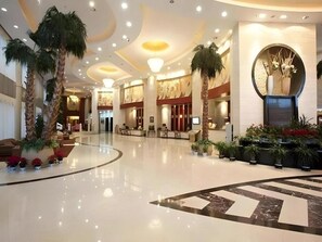 A spacious lobby with a polished floor, palm trees, and a reception desk.