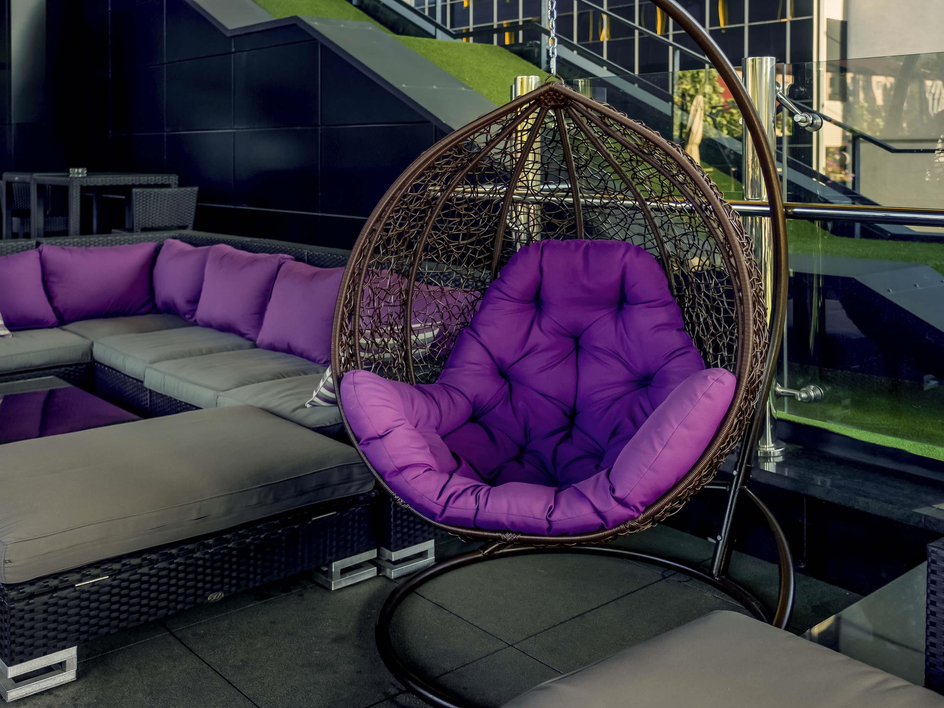 Un espace extérieur moderne aménagé avec des sièges, comprenant un fauteuil suspendu et un canapé.