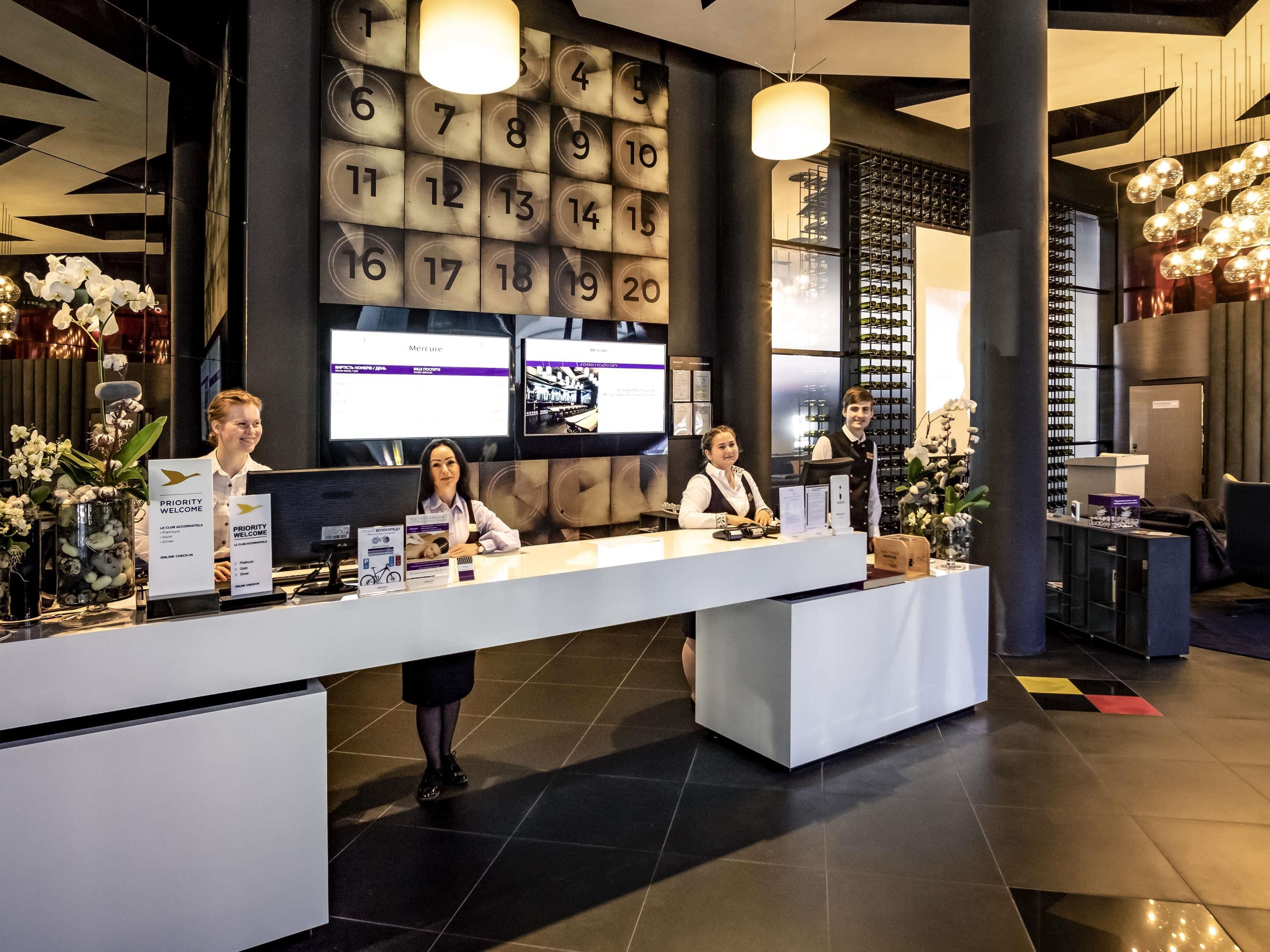 A reception desk with a modern design, featuring a digital display, a clock, and a wine rack in the background.
