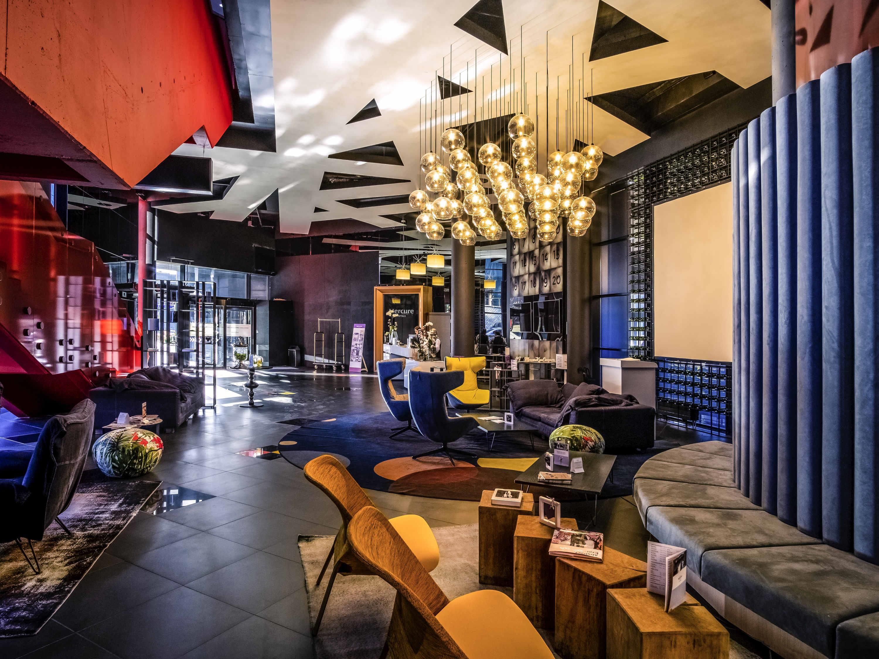 A modern hotel lobby with a central seating area, a reception desk, and a large chandelier.