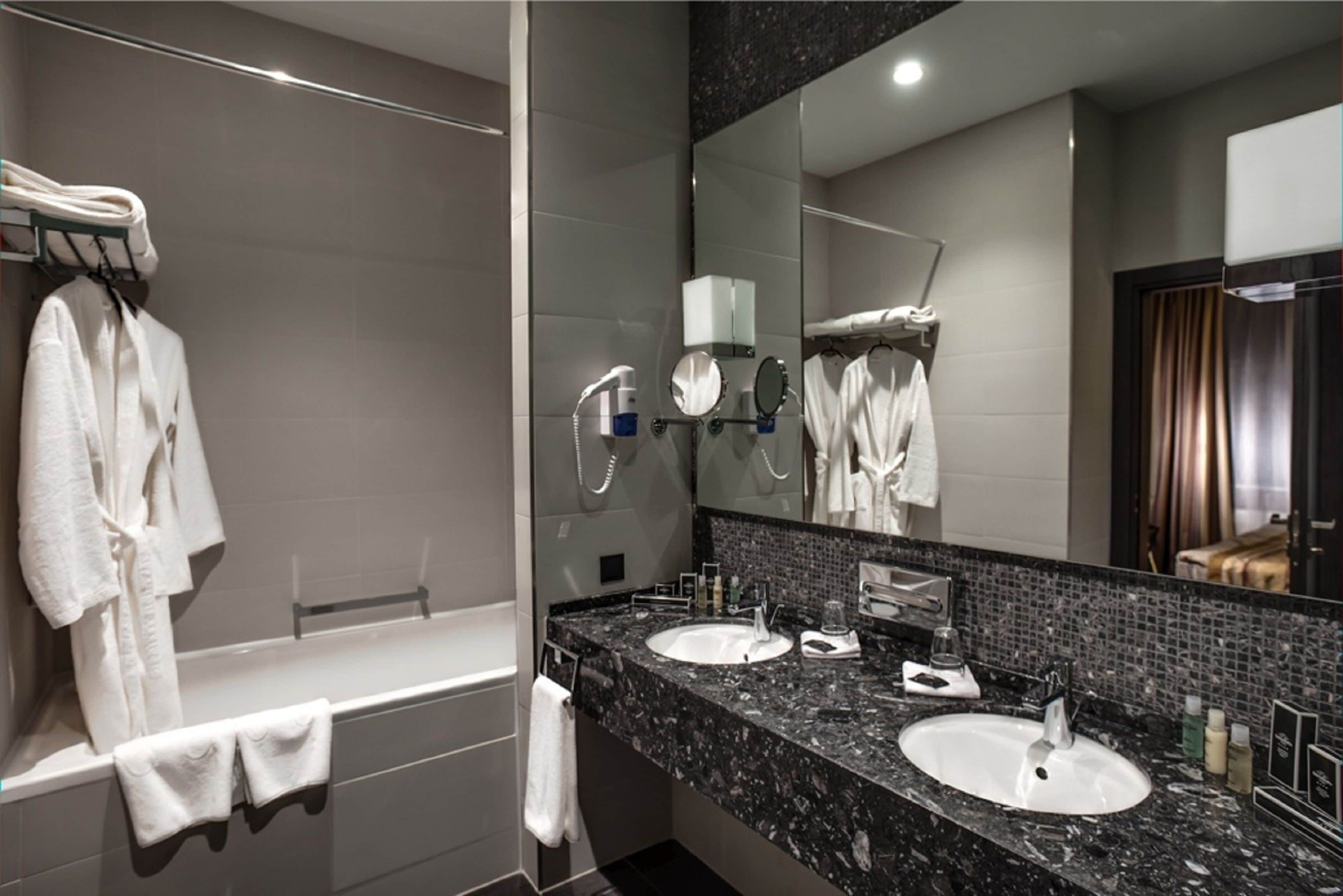 A modern bathroom with two sinks, a large mirror, and a bathtub.