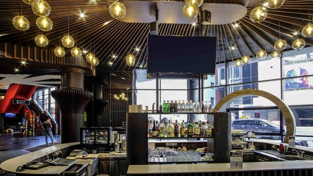 A modern bar with a curved counter, a large TV screen, and a variety of liquor bottles. - Mercure Kyiv Congress (Kyiv)