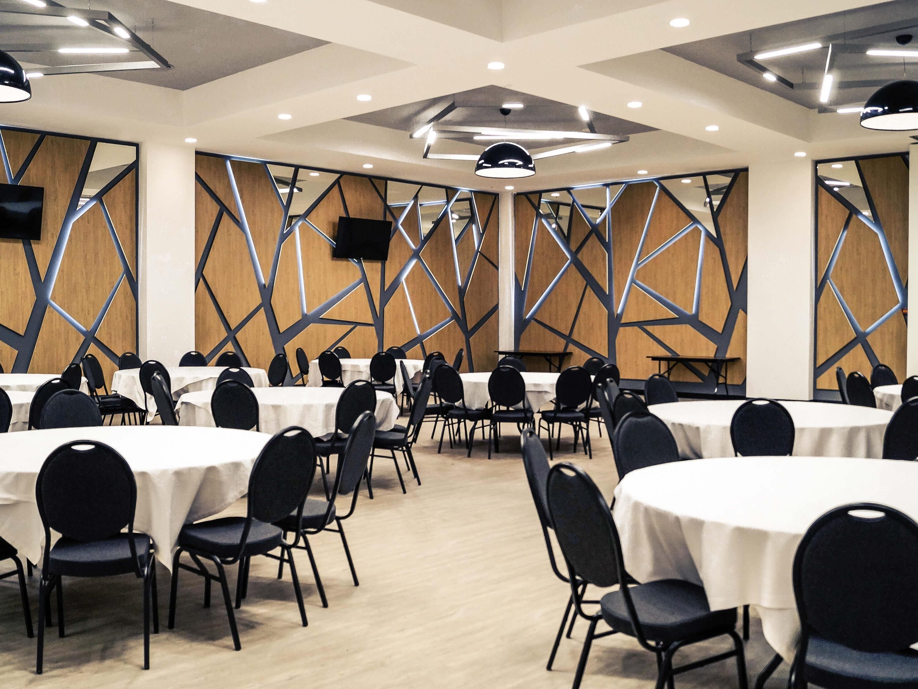 A conference room with multiple tables and chairs, geometric wall designs, and ceiling lights.