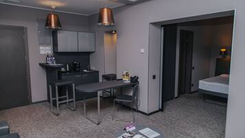 Una habitación de hotel compacta con kitchenette, comedor y zona de descanso separada.