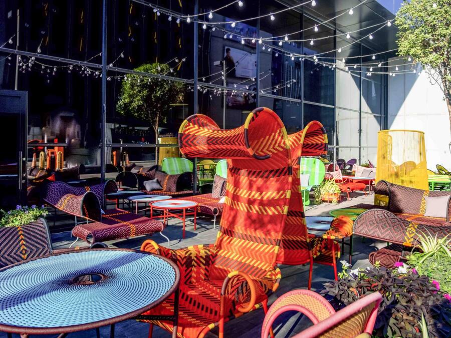 An outdoor seating area with various chairs and tables, some with colorful woven patterns.