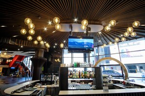 A modern bar area with a curved counter, a large TV screen, and a variety of bottles and glasses. - Mercure Kyiv Congress (Kyiv)