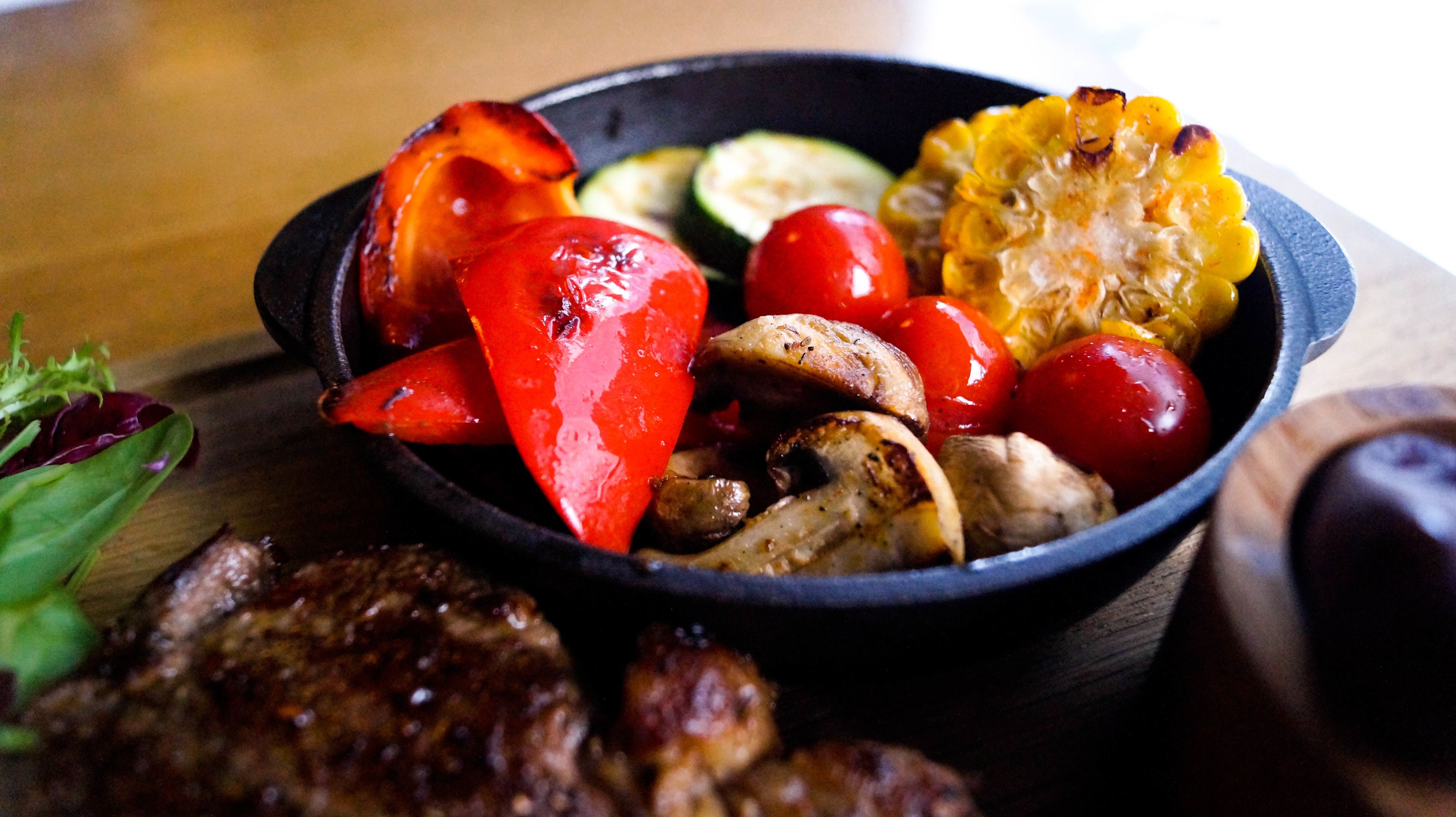 A bowl of grilled vegetables and meat on a wooden table.