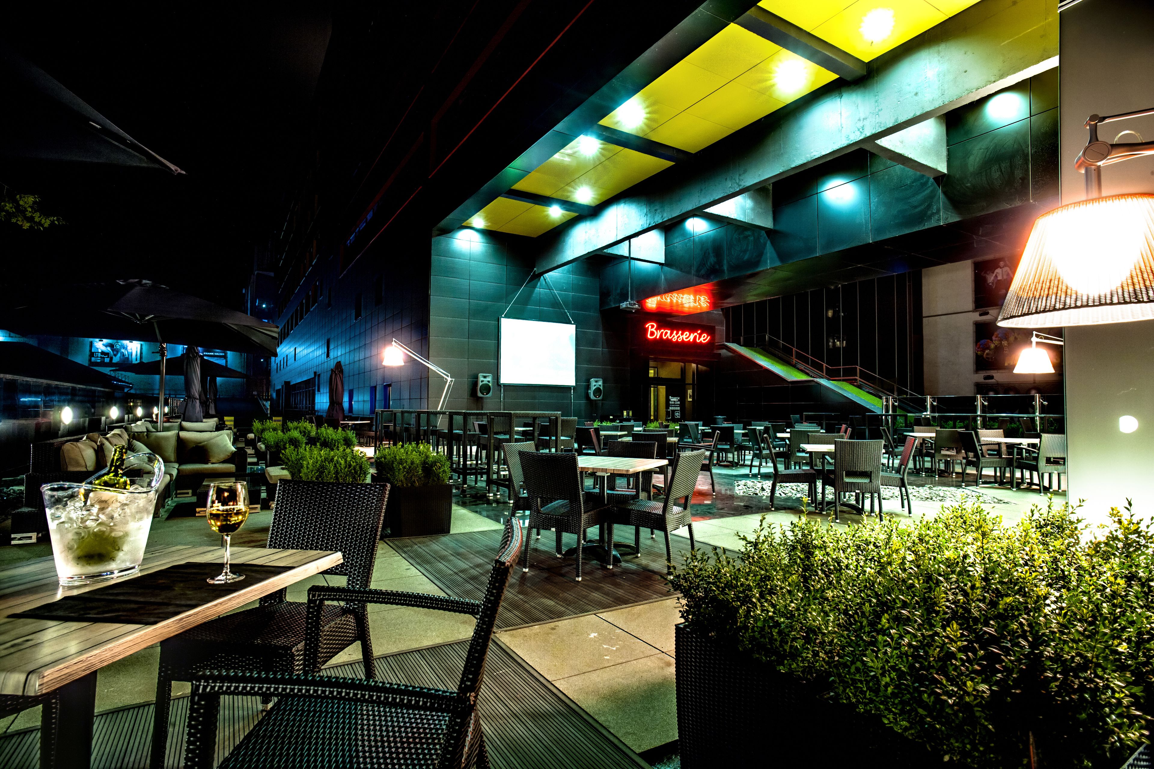 An outdoor dining area with tables and chairs, a neon sign, and a modern architectural ceiling.