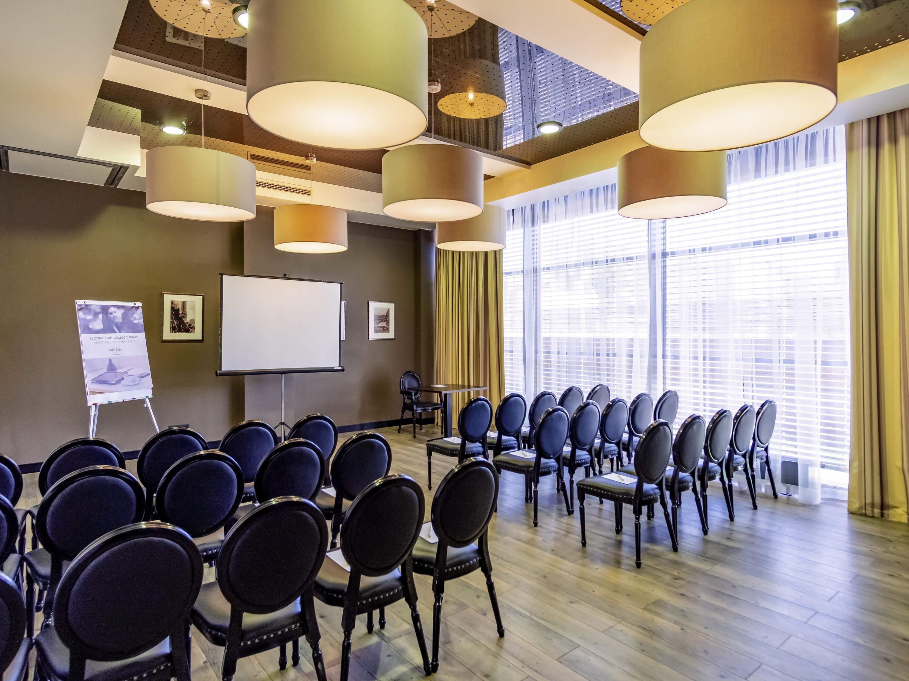 A conference room with rows of chairs, a whiteboard, and a projector screen.