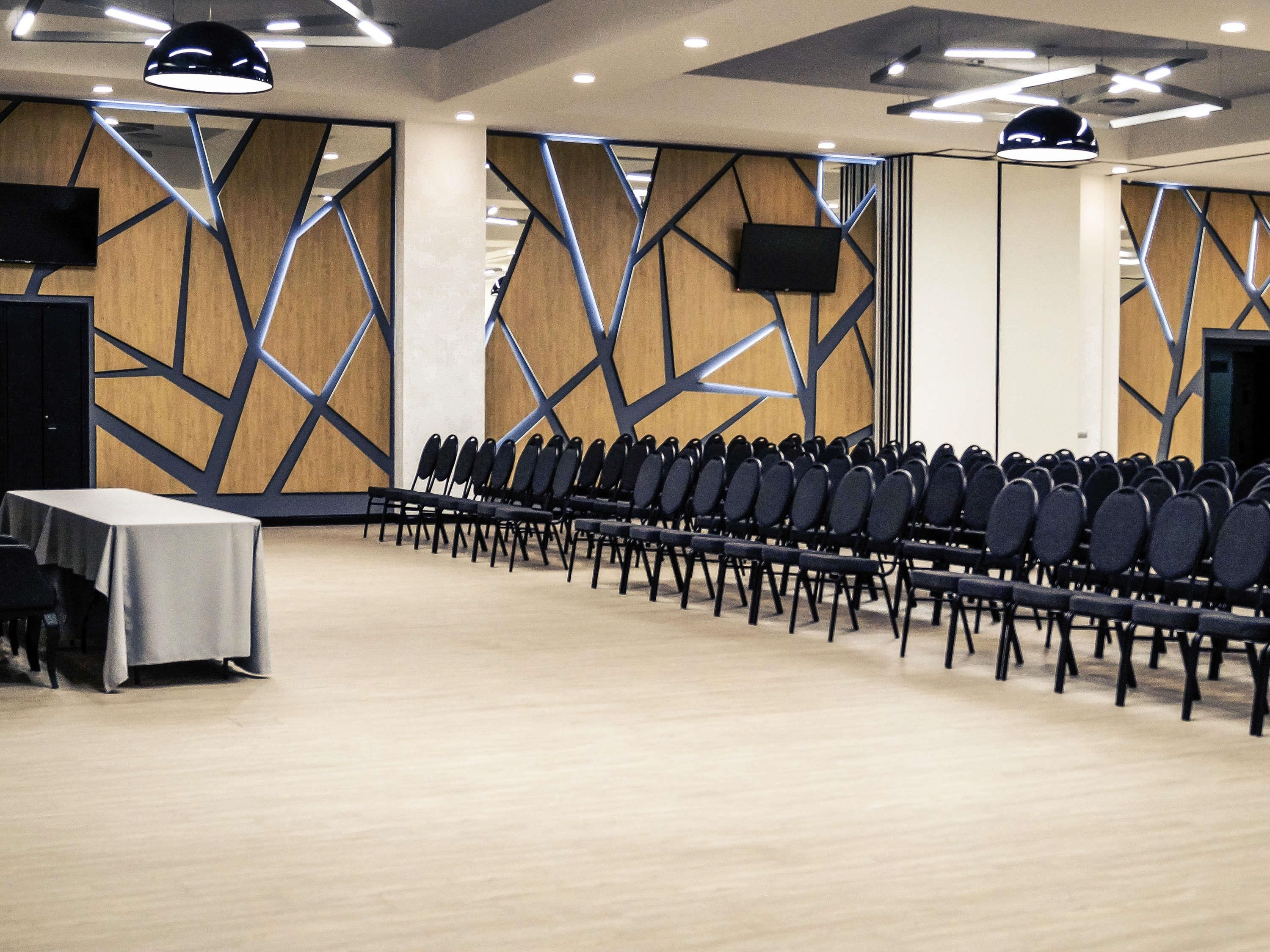 Un salón de conferencias con filas de sillas, una mesa y un diseño moderno de pared geométrico.