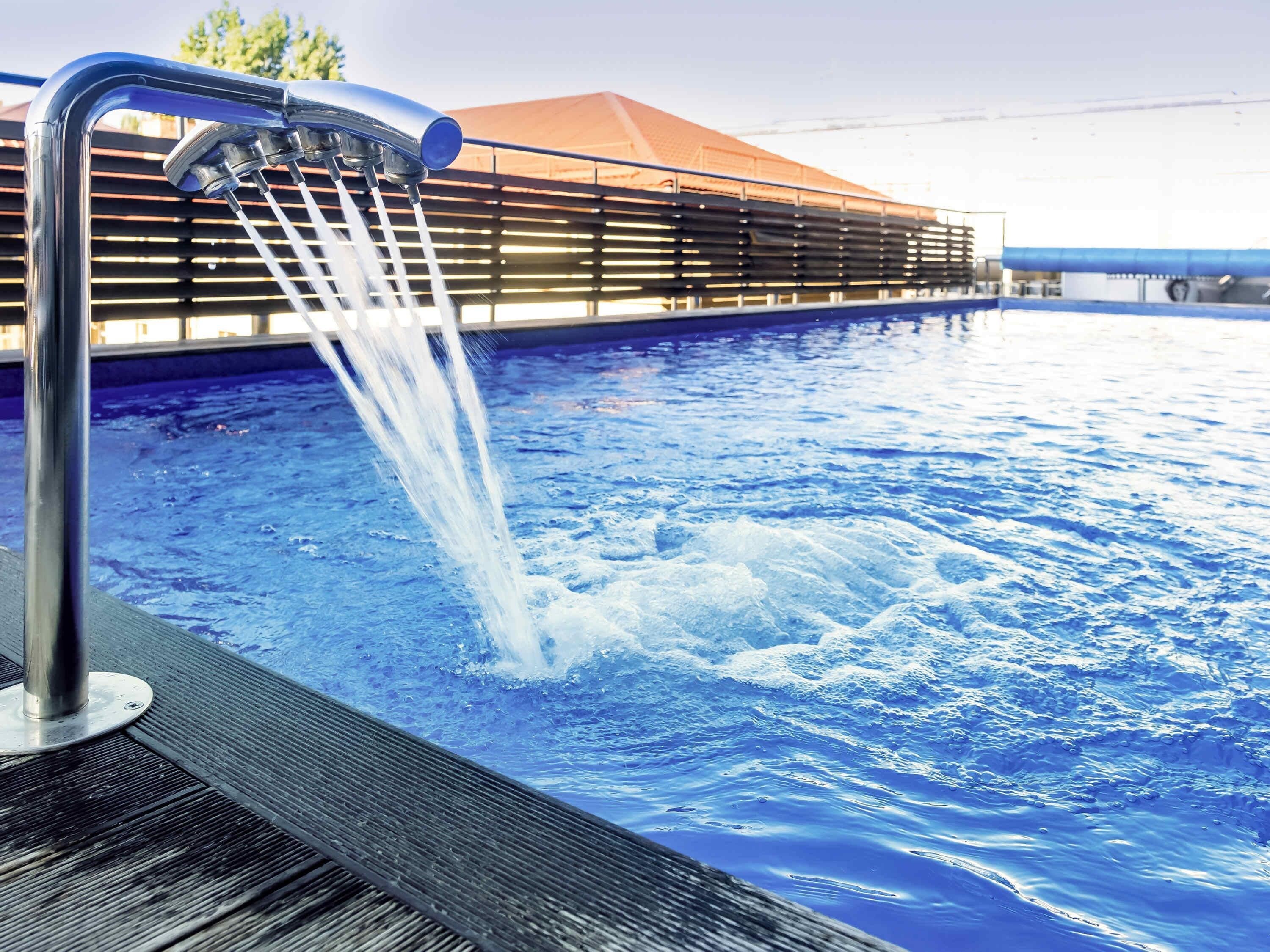 A swimming pool with a water fountain feature, surrounded by a wooden deck and a covered area.