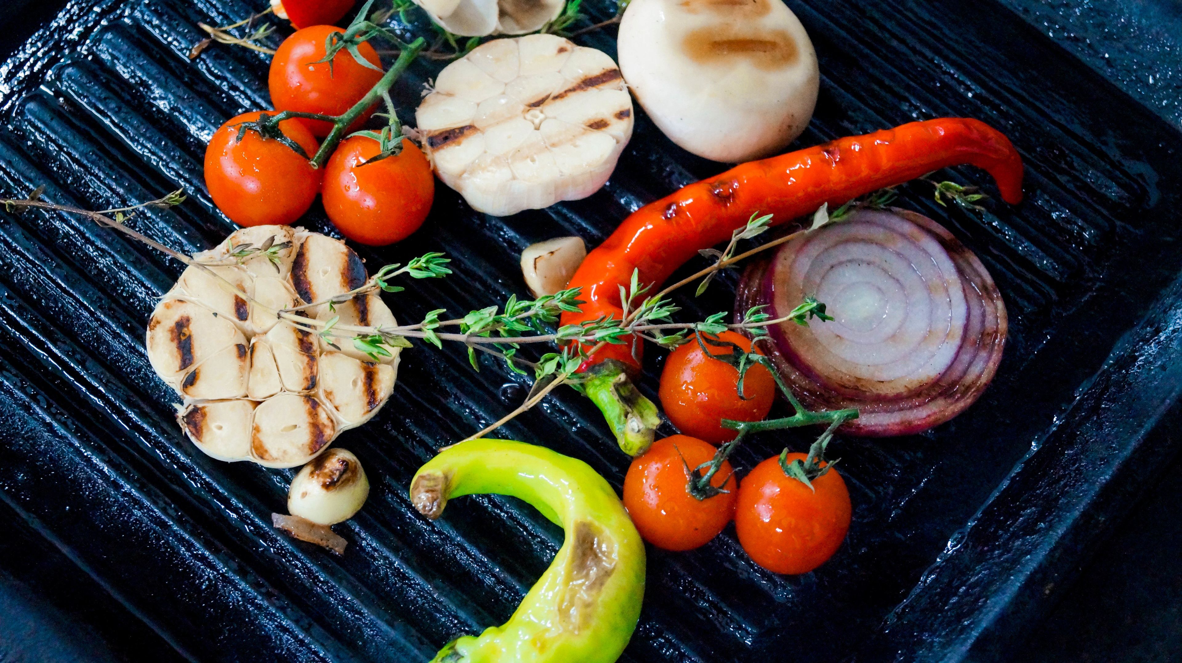 Variedad de verduras a la parrilla, incluyendo tomates, pimientos, cebollas y ajo.