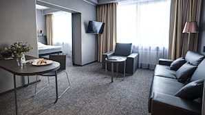 A hotel room with a bed, a dining table with a plate of food, a sofa, a small table, and a TV mounted on the wall. - Mercure Kyiv Congress (Kyiv)