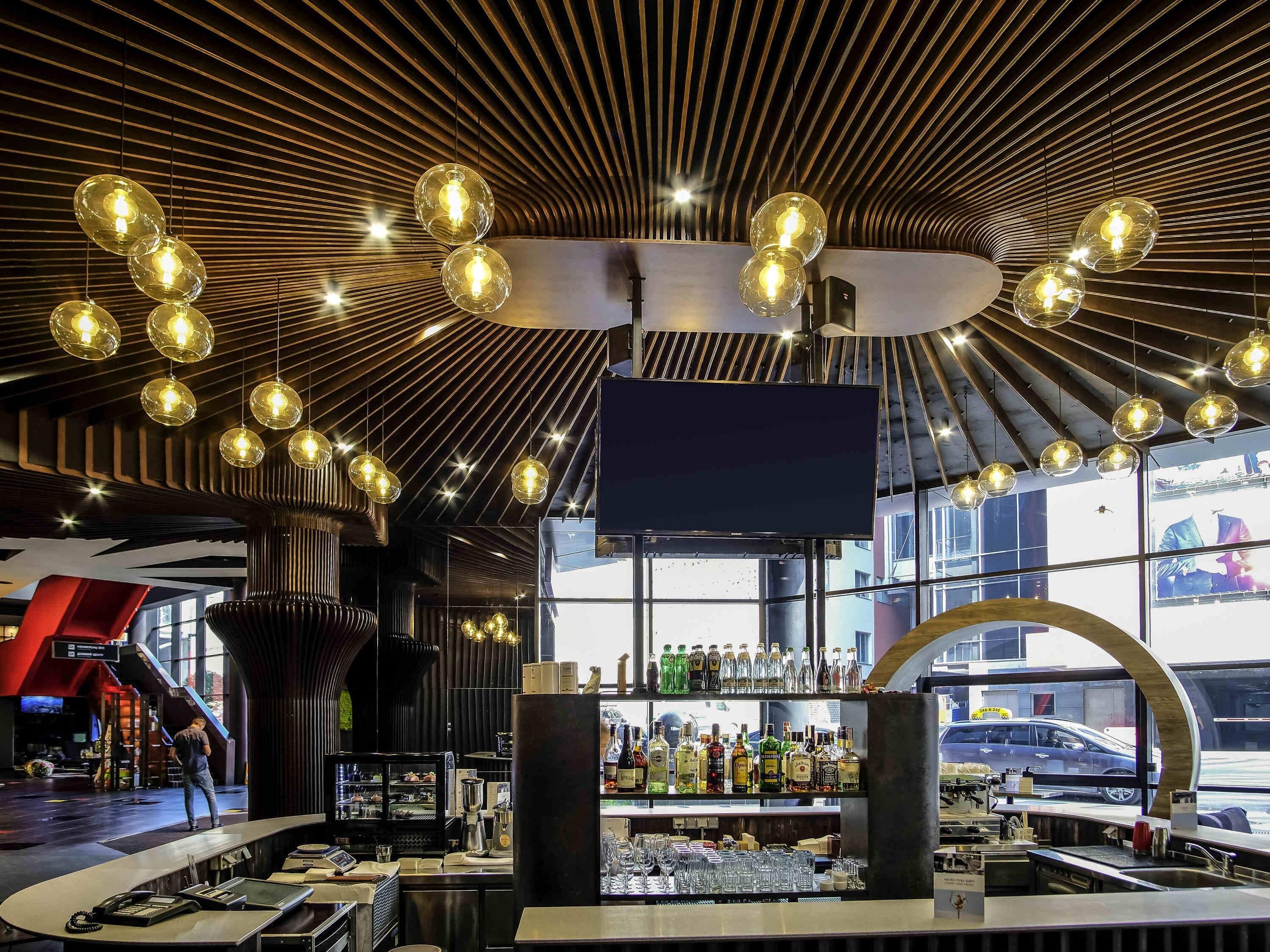 Un bar moderno con una barra curva, una pantalla de televisión grande y una variedad de botellas de licores.