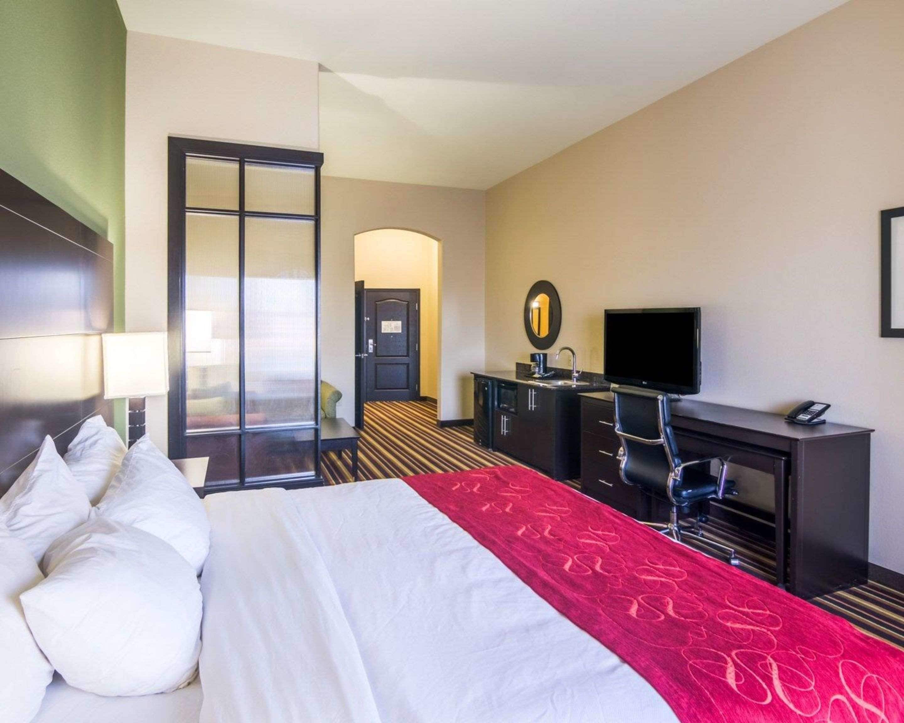 Habitación de hotel con cama, escritorio, televisión y baño visible a través de una puerta abierta.