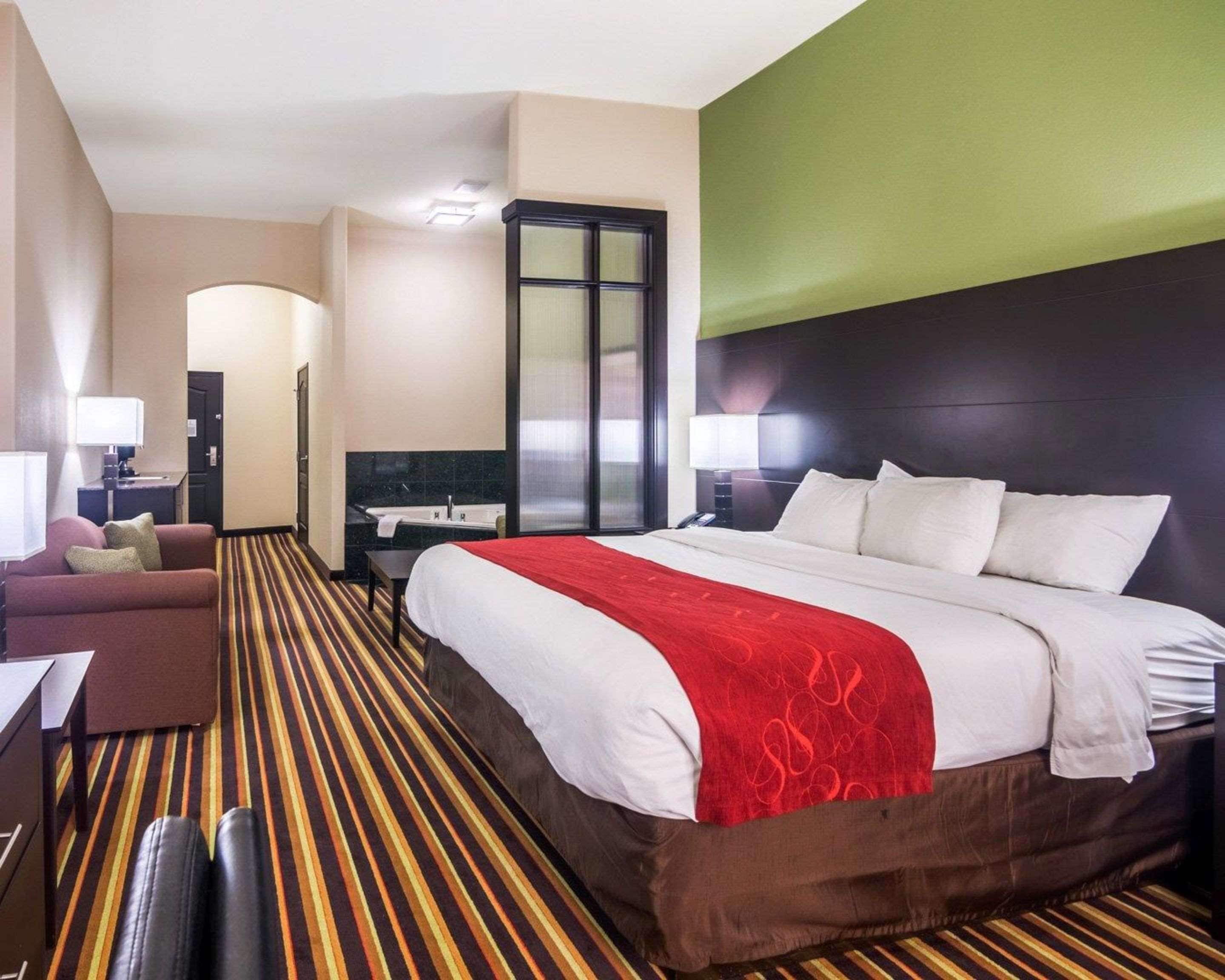 A hotel room with a large bed, a desk with a chair, a sofa, and a bathroom with a bathtub.