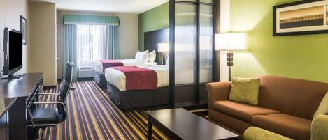 A hotel room with two beds, a sofa, a desk with a chair, a TV, and a lamp.