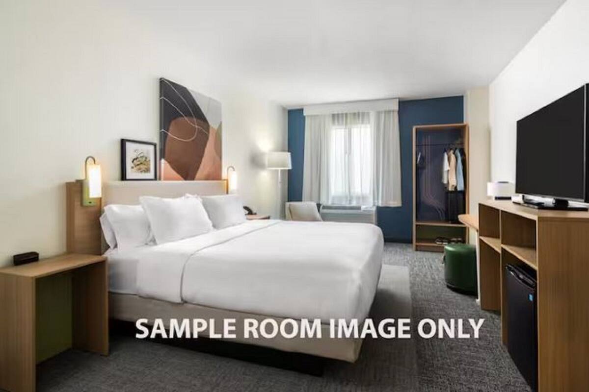 A hotel room with a bed, bedside tables, a TV, a wardrobe, and a window with curtains.