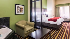 Habitación de hotel con pared verde, un cuadro enmarcado, cama con manta roja, una silla, una mesita y alfombra a rayas.