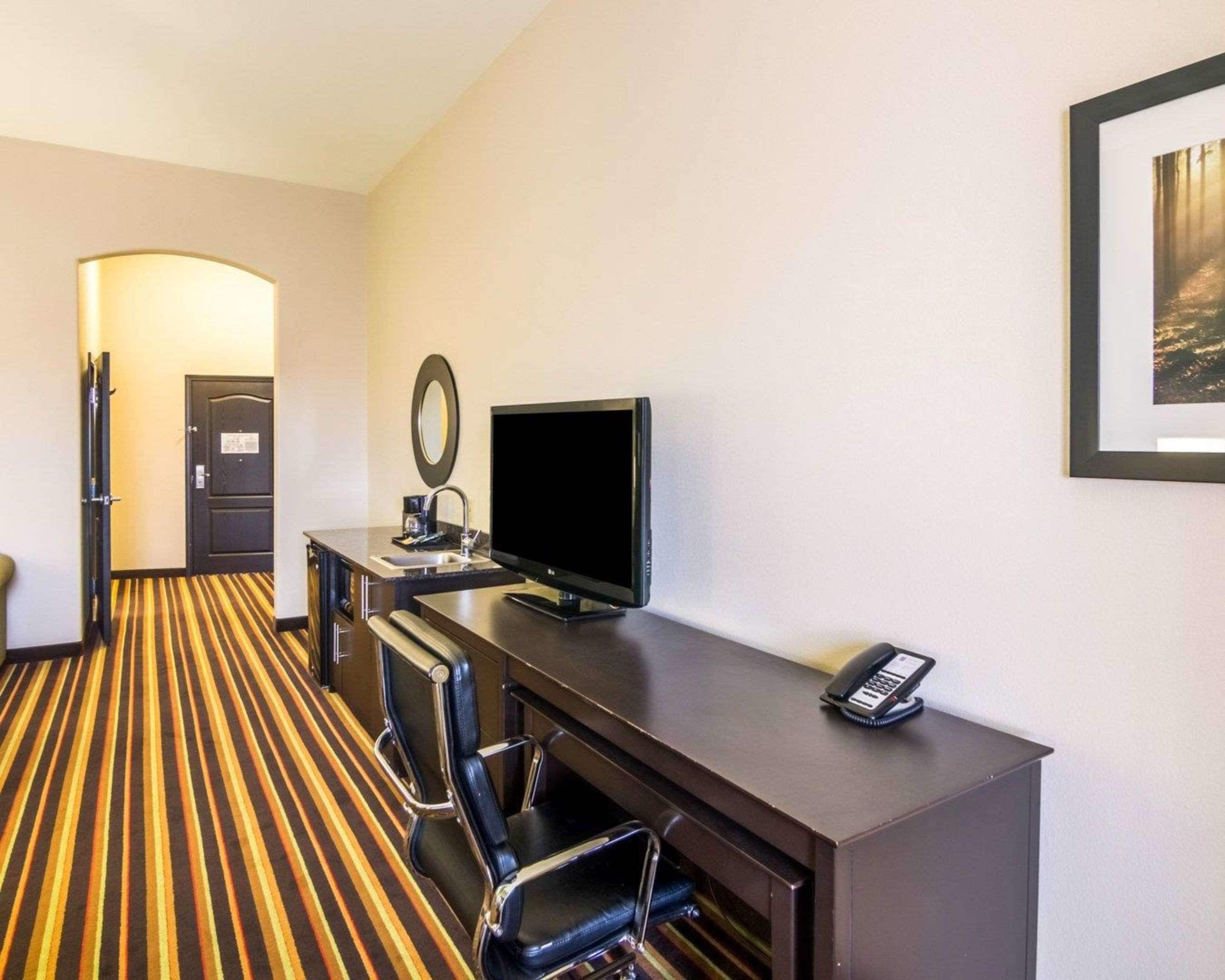A hotel room with a striped carpet, a desk with a flat-screen TV, a telephone, and a mirror.